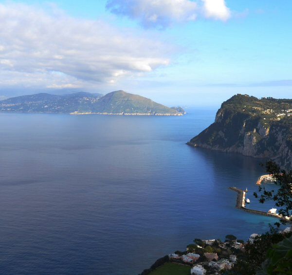 Vue imprenable depuis les hauteurs de Capri sur le port de Marina Grande et la silhouette de la côte au loin.