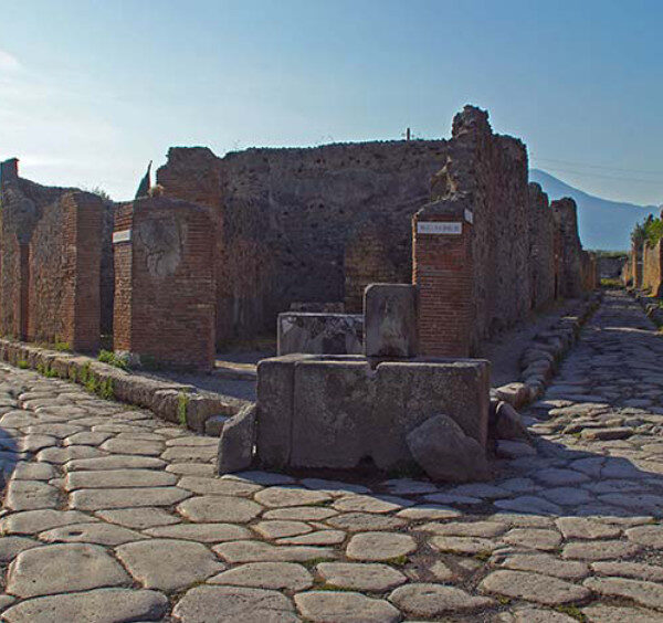 Rues pavées antiques et ruines de maisons à Pompéi avec le Vésuve en arrière-plan.