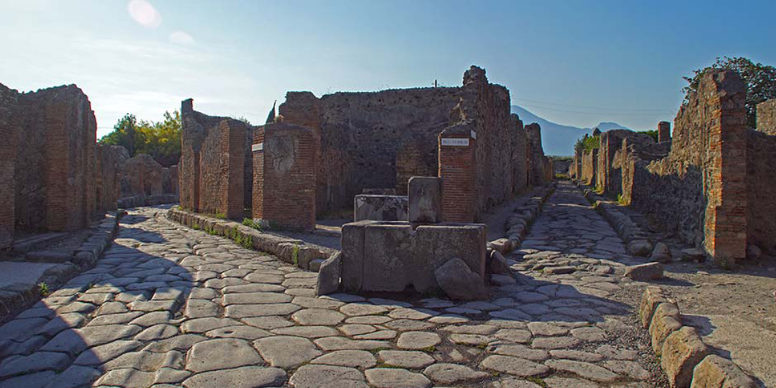 Rues pavées antiques et ruines de maisons à Pompéi avec le Vésuve en arrière-plan.